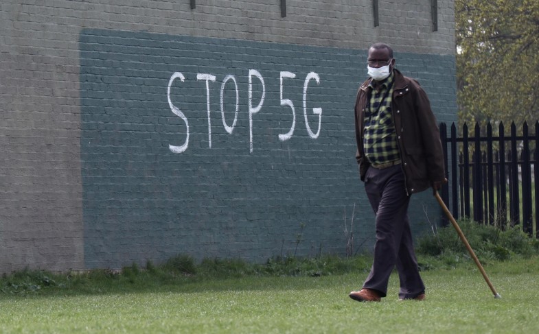 A man wearing a face mask during an outbreak of coronavirus disease (COVID-19) walks past a graffiti that reads «STOP 5G» in London